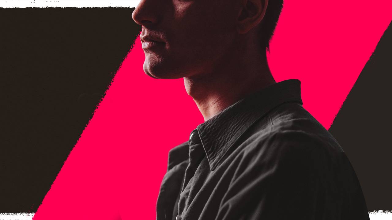 Alt text: Partially visible side profile of a person wearing a dark button-up shirt, standing against a bold pink geometric background. The person’s face is mostly cropped, with dramatic lighting creating a high-contrast, stylized portrait.