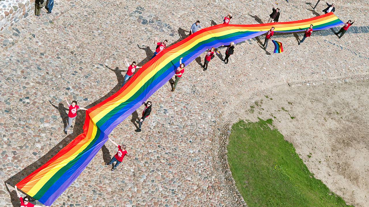 Long rainbow flag held by people in a line