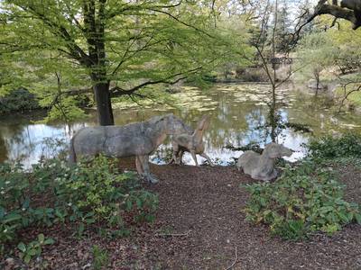 A lakeside scene in Crystal Palace Park with a tree in the foreground beside statues of prehistoric animals.