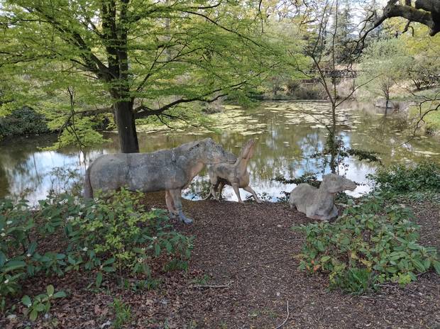 A lakeside scene in Crystal Palace Park with a tree in the foreground beside statues of prehistoric animals.